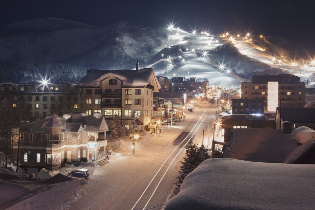 High level view of a ski resort at night in Niseko, Japan with a mountain in the distance and ski town in the foreground.